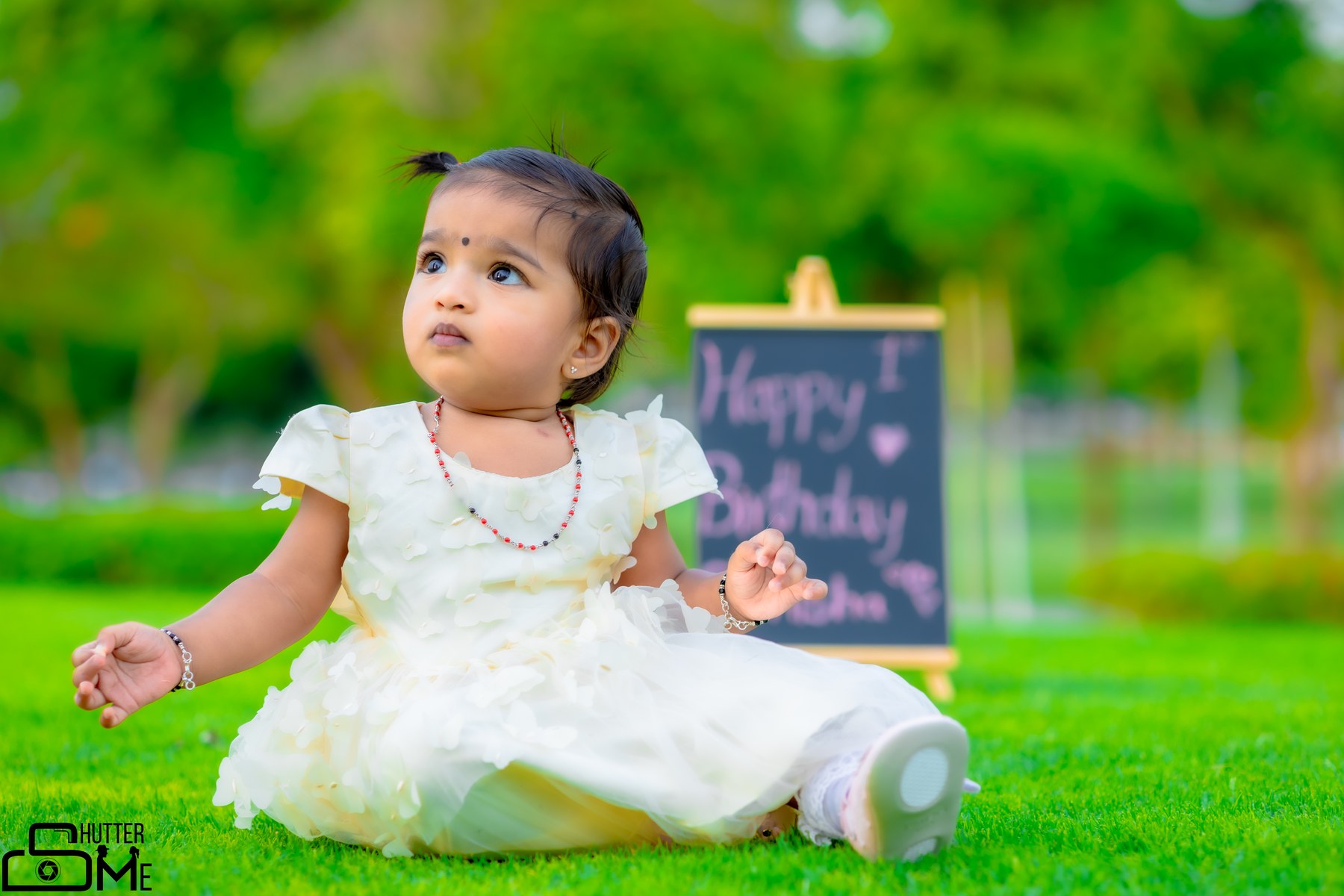 Child in a white dress sitting in a green garden